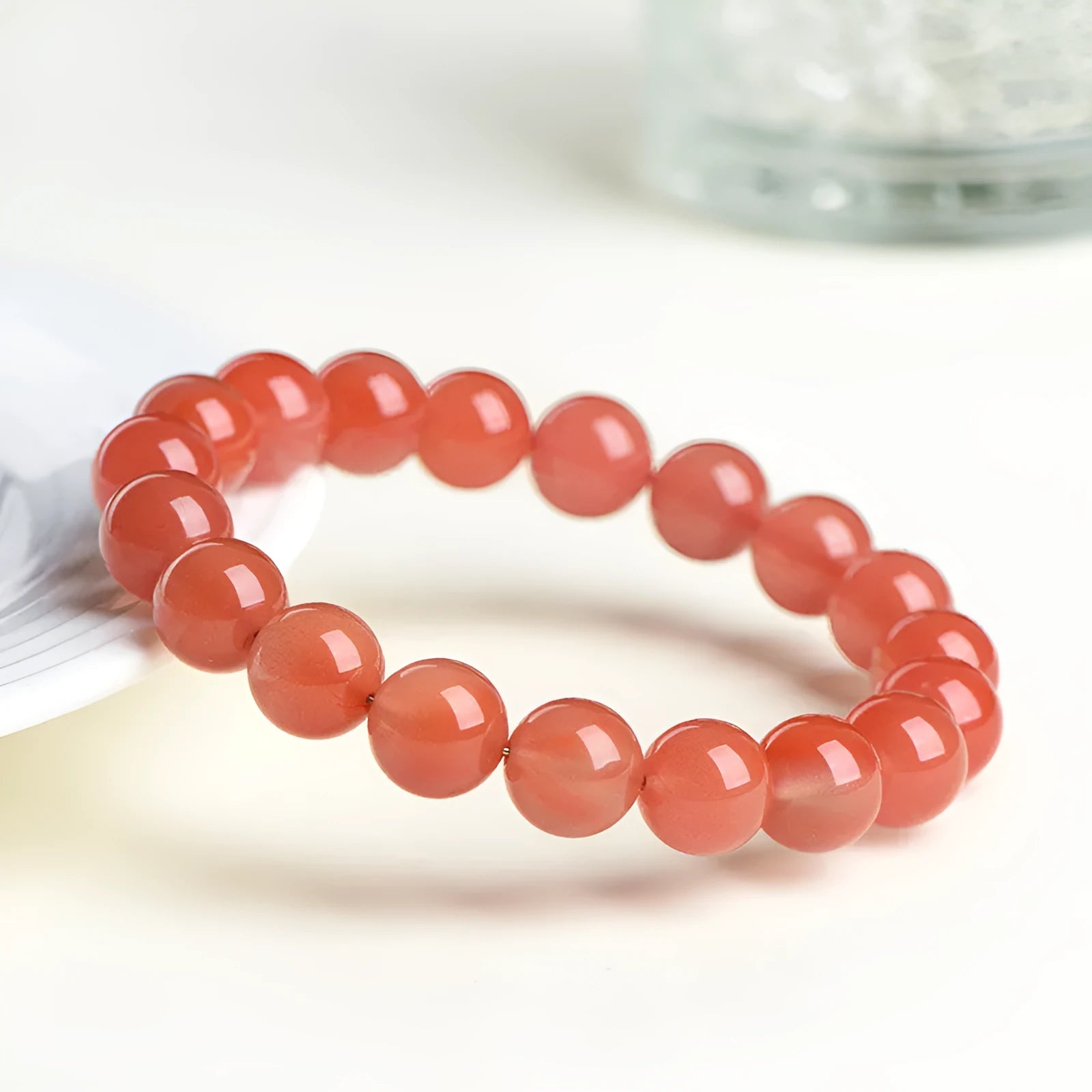 Scattered polished cherry red agate beads and elastic cord for a DIY bracelet next to an assembled single-strand bracelet.