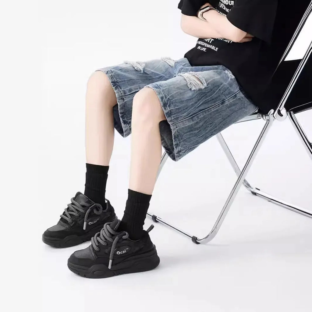 Man wearing loose-fit black denim shorts with ripped detailing and a washed vintage finish.
