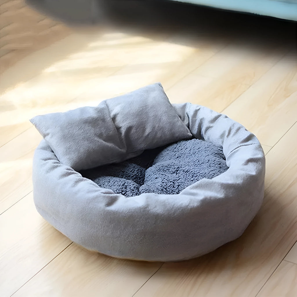 Grey round pet bed with raised rim and pillow for small dogs or cats on a wooden floor.