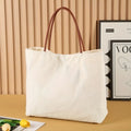 Beige white canvas tote bag with top handles and an internal zip pocket, shown with a book and keys.