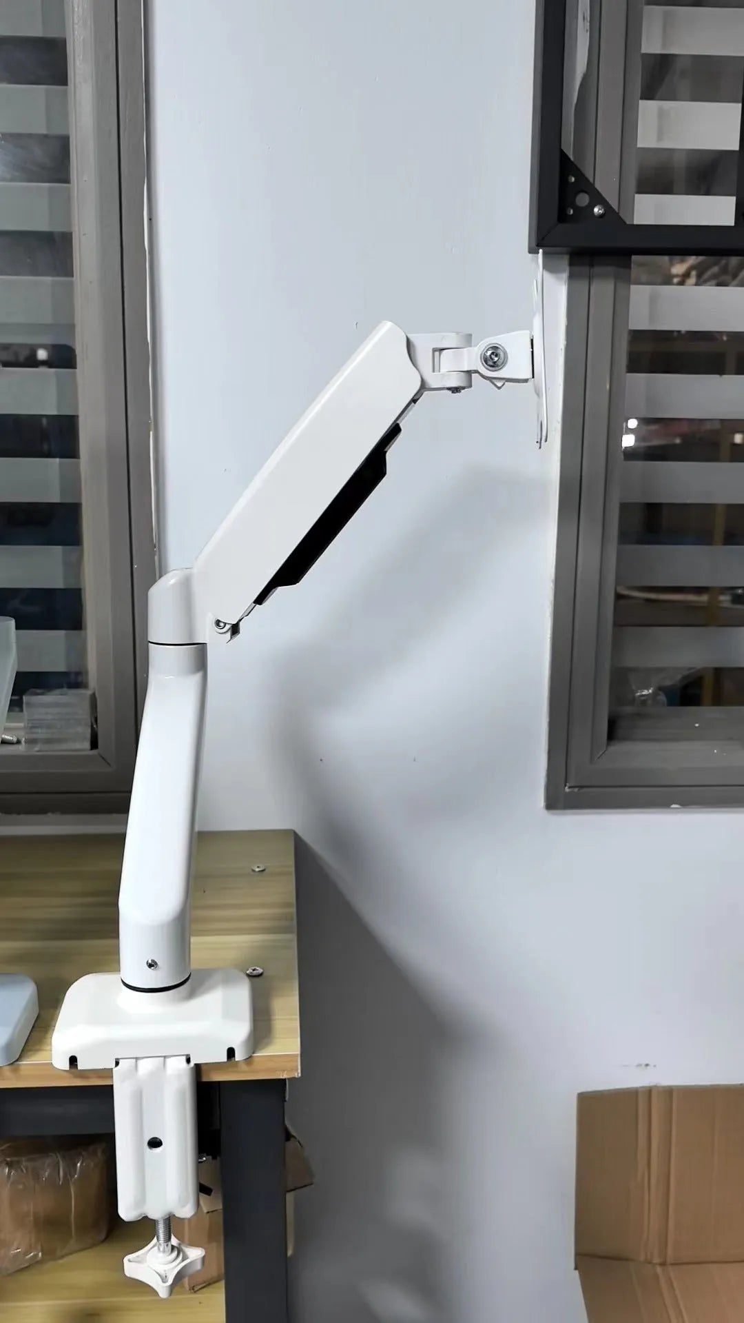 Black adjustable LCD monitor desk bracket extended beside a white version on a wooden desk.